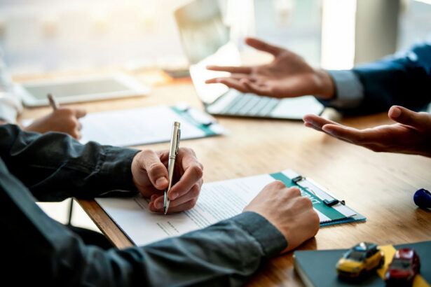 Three people in a meeting room discuss documents at a wooden table. One holds a pen over paper, others gesture expressively, conveying an engaged discussion.