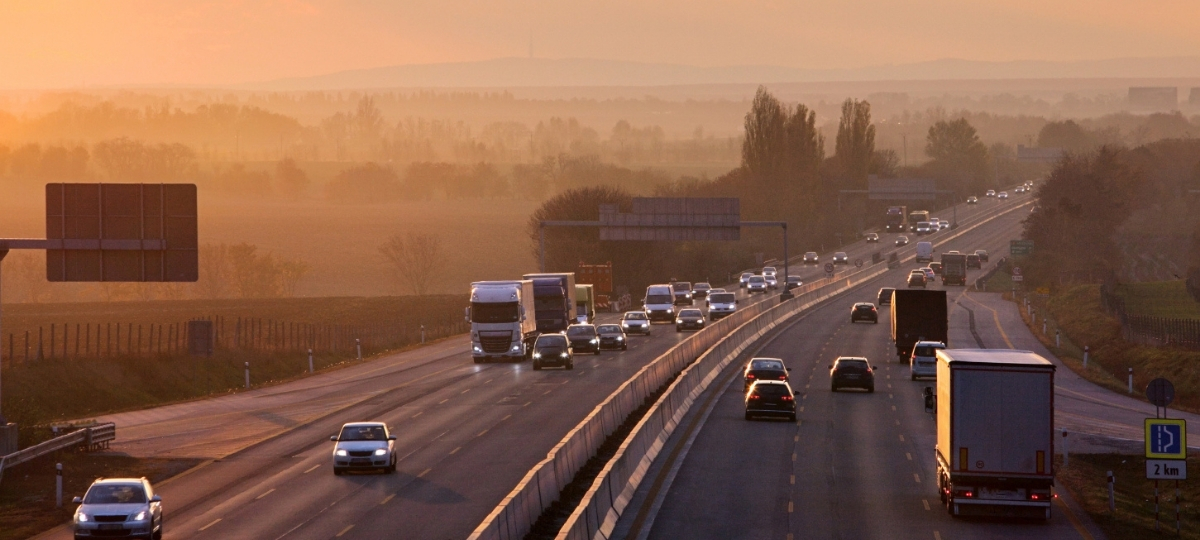 Traffic moves along a highway at sunset, with trucks and cars travelling through a hazy rural landscape.