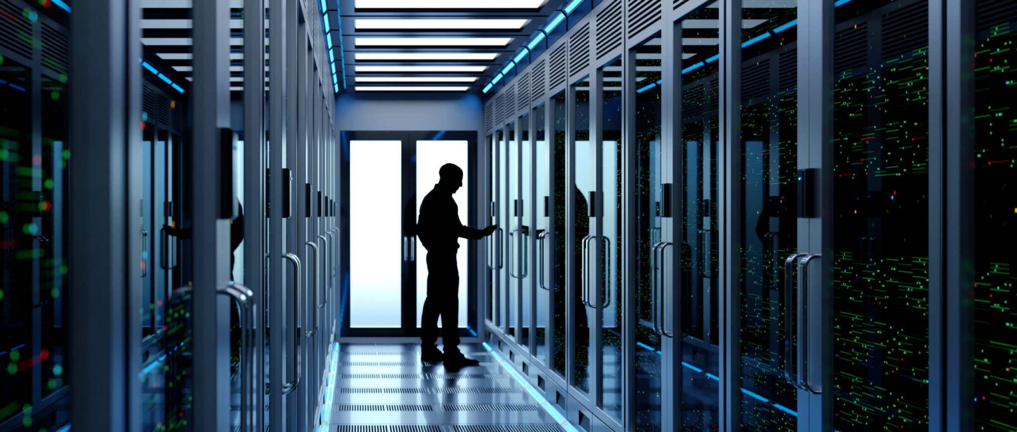 A person stands in a hallway lined with server racks, interacting with equipment in a modern data centre.