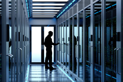A person stands in a hallway lined with server racks, interacting with equipment in a modern data centre.