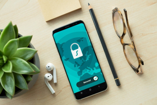 A mobile phone with a padlock on the lockscreen sitting on a table with a pencil and pair of glasses.