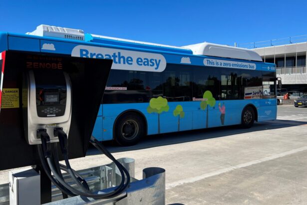 A blue zero-emissions bus is parked beside a Zenobē electric charging unit, with charging cables connected in a depot setting.