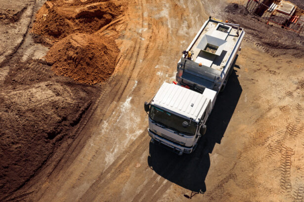 Aerial view of a utility truck driving through a construction site, surrounded by earthworks, excavated soil and heavy vehicle tracks, illustrating field operations and remote asset management.