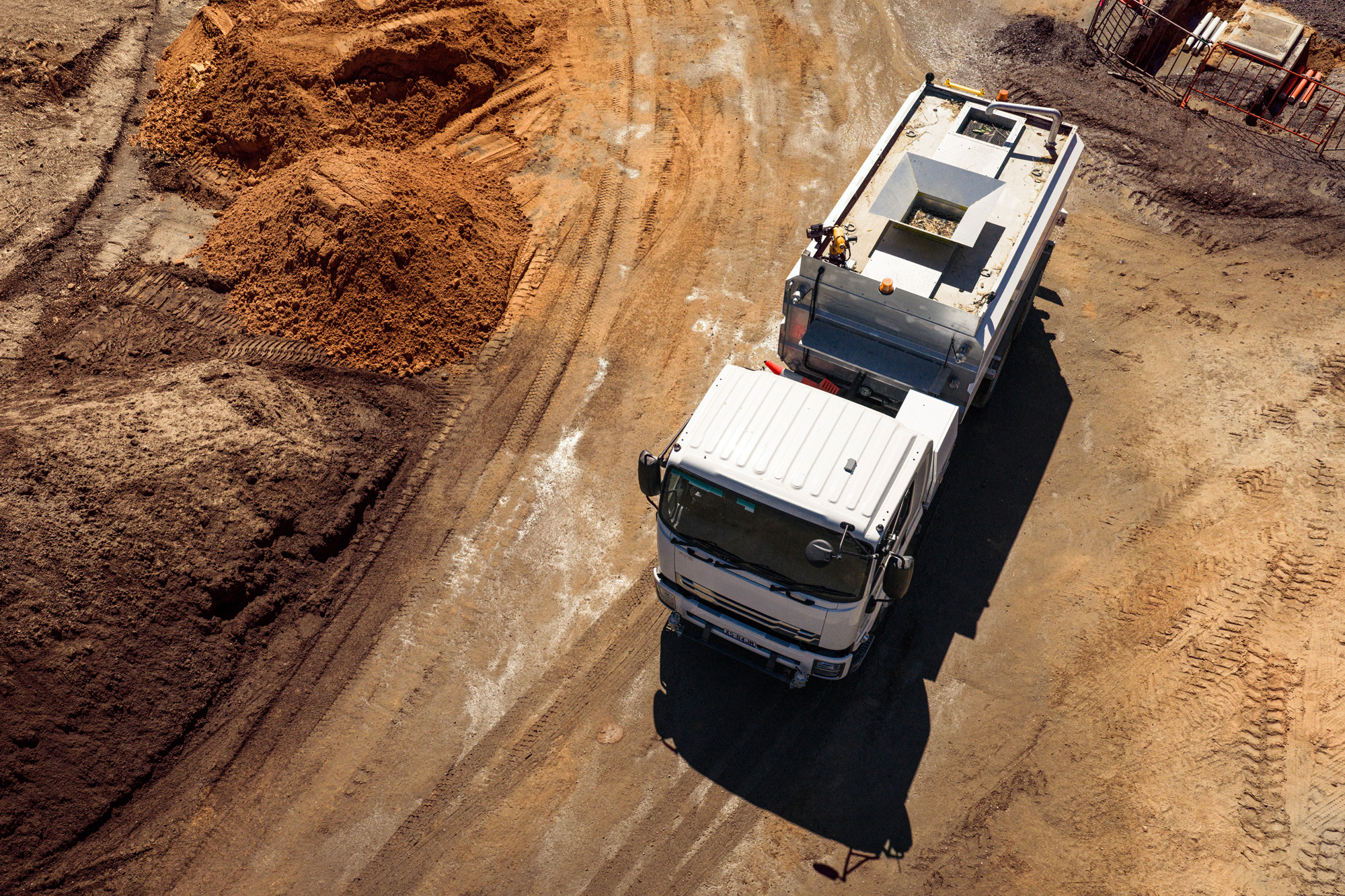 Aerial view of a utility truck driving through a construction site, surrounded by earthworks, excavated soil and heavy vehicle tracks, illustrating field operations and remote asset management.