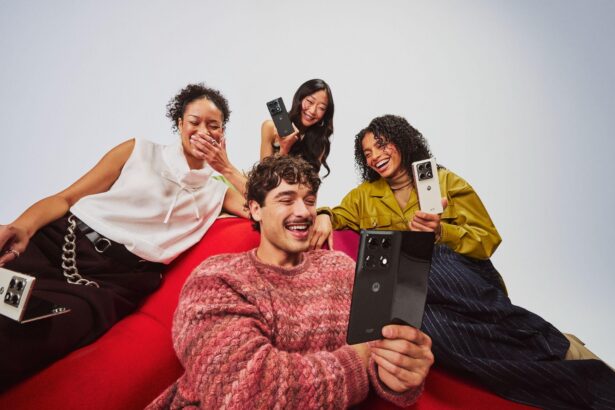 Four people sitting together on a red couch smile and laugh while holding Motorola razr smartphones in different colours, showcasing the devices' foldable design during a group selfie.