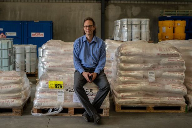 A man in a blue shirt sits on stacked pallets of wrapped goods.