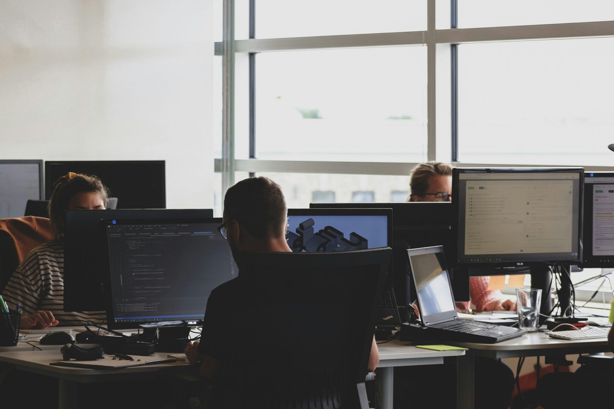 Three people sitting on office chairs looking at computer monitors.