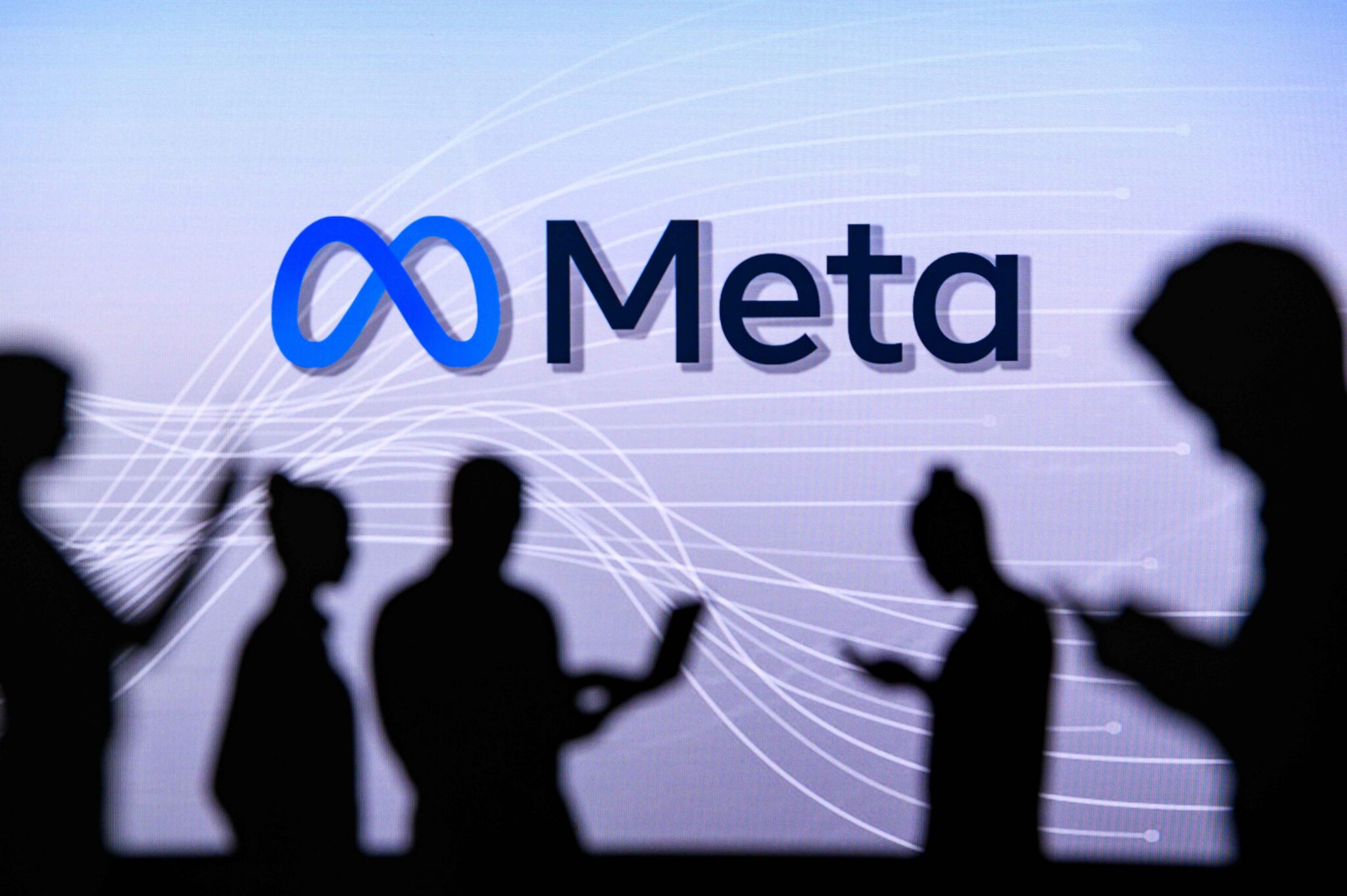 Silhouettes of people using smartphones in front of a large Meta logo displayed on a digital screen, illustrating the social media company's platforms and online services.