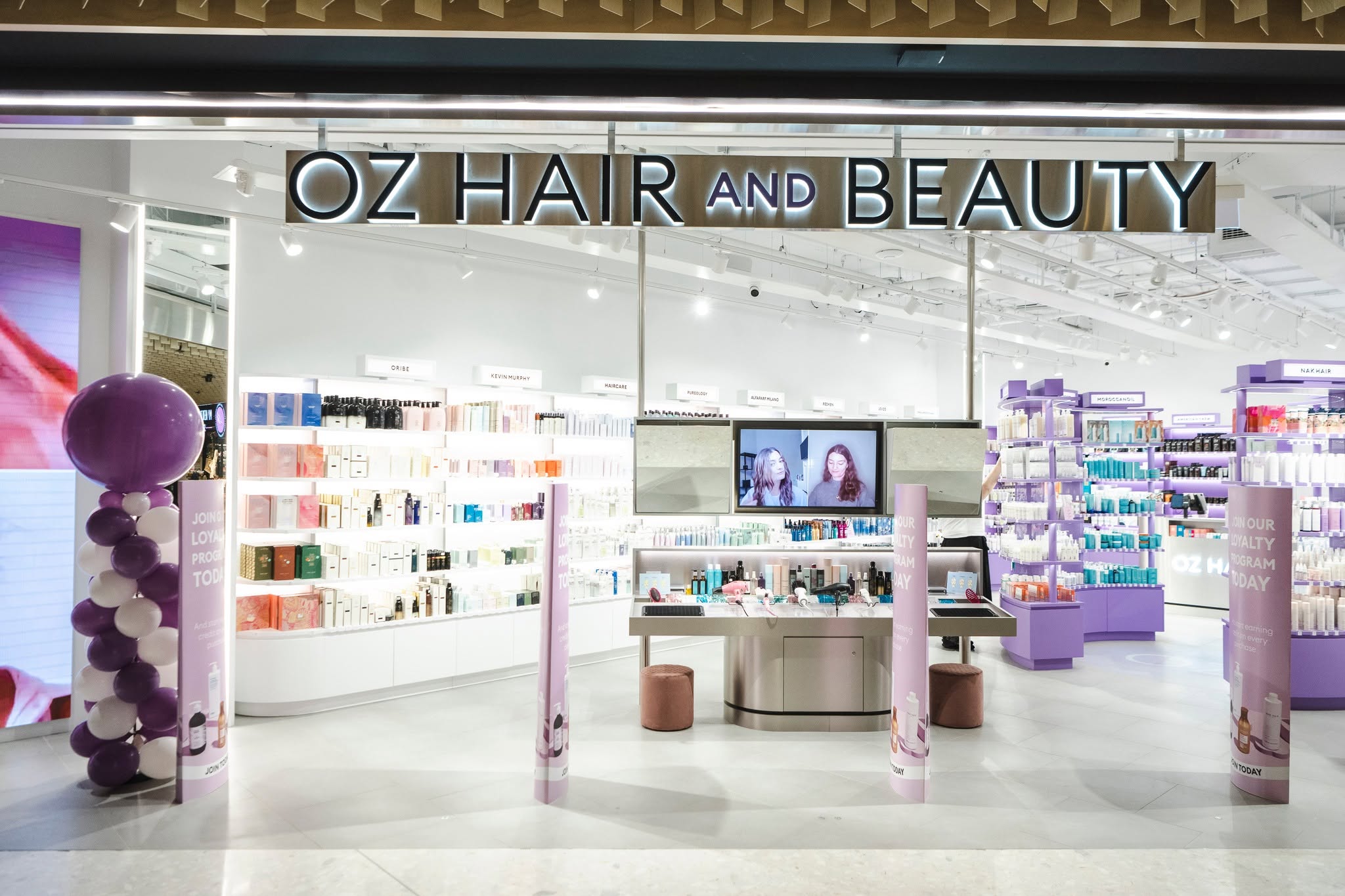 Interior of an Oz Hair and Beauty store, with brightly lit shelves displaying hair and beauty products around a central service counter.