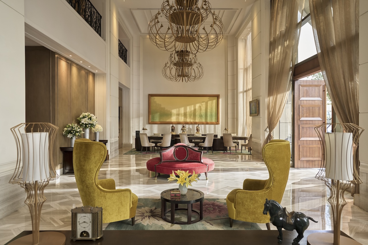Elegant hotel lobby with high ceilings, chandeliers, floor-to-ceiling windows and colourful lounge seating.