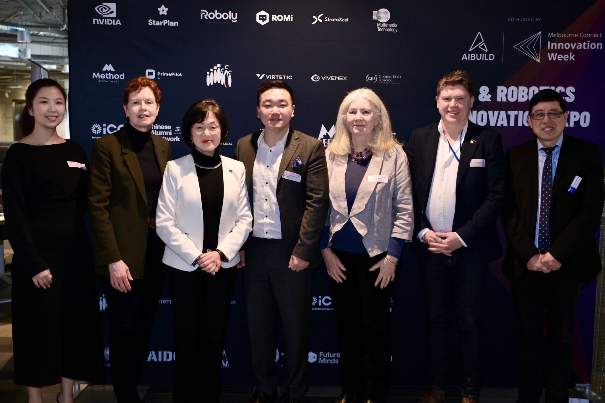 Seven attendees pose for a group photo in front of the AI & Robotics Innovation Expo backdrop during Melbourne Innovation Week.