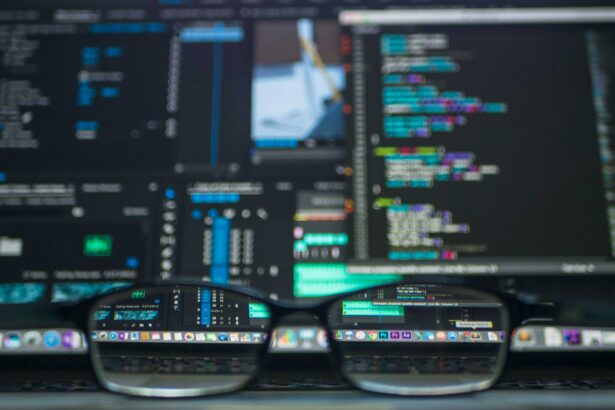Close-up of a pair of glasses resting on a laptop keyboard, reflecting colourful computer screens displaying code and editing software.