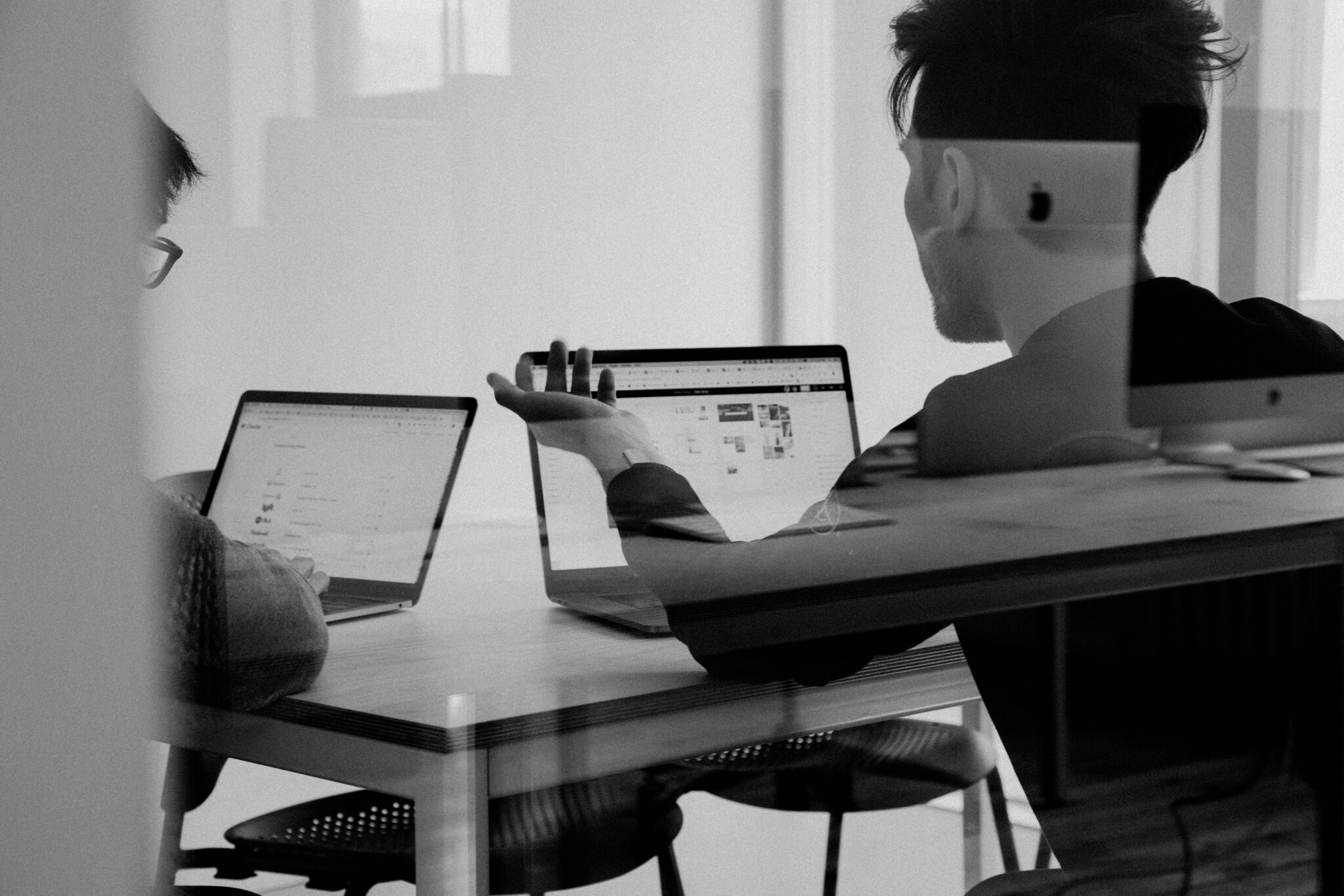 Two people sit at a table and work on their macbook laptops.