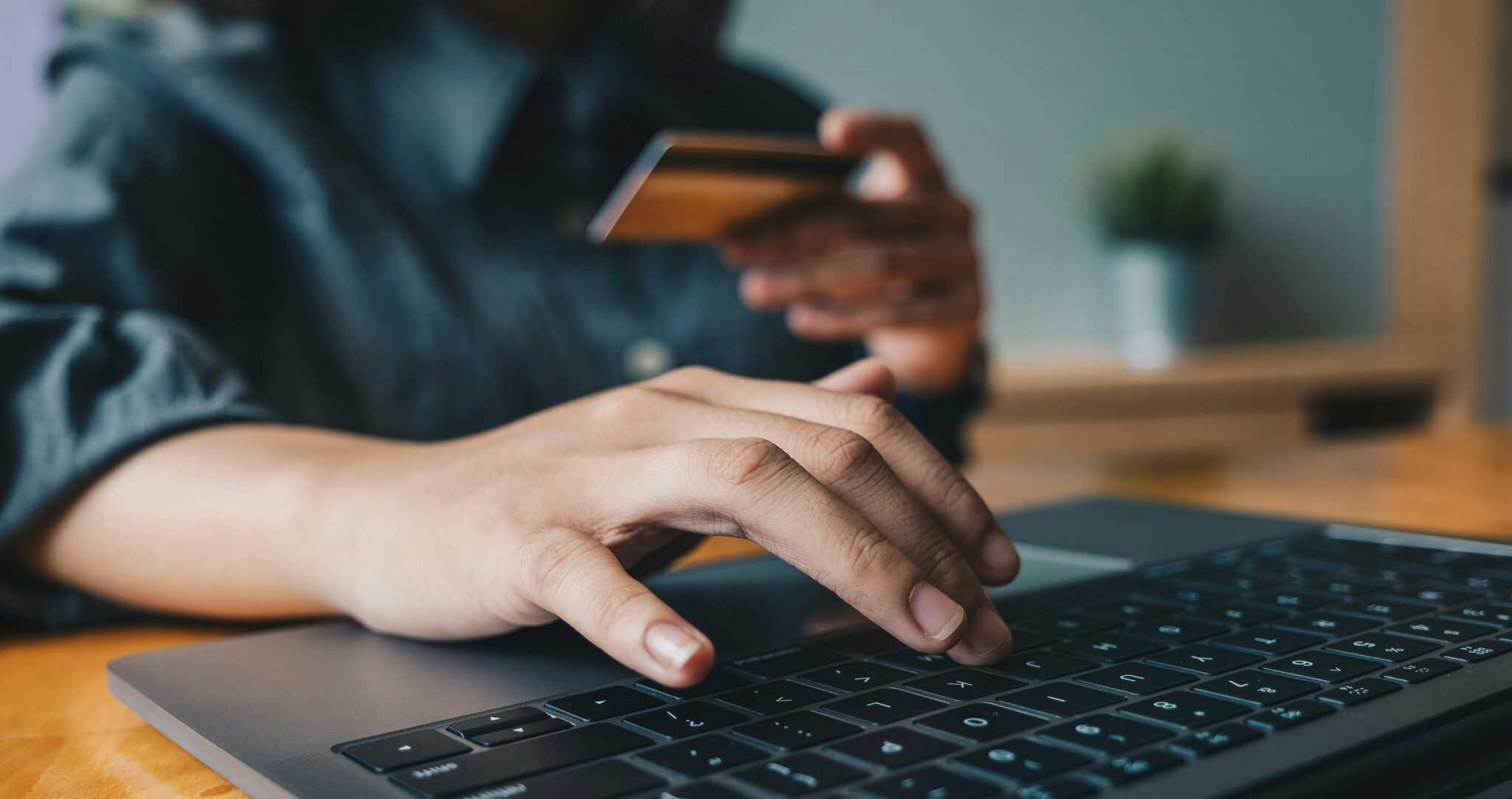 Close-up of a person typing on a laptop while holding a credit card, illustrating online shopping and digital payments.